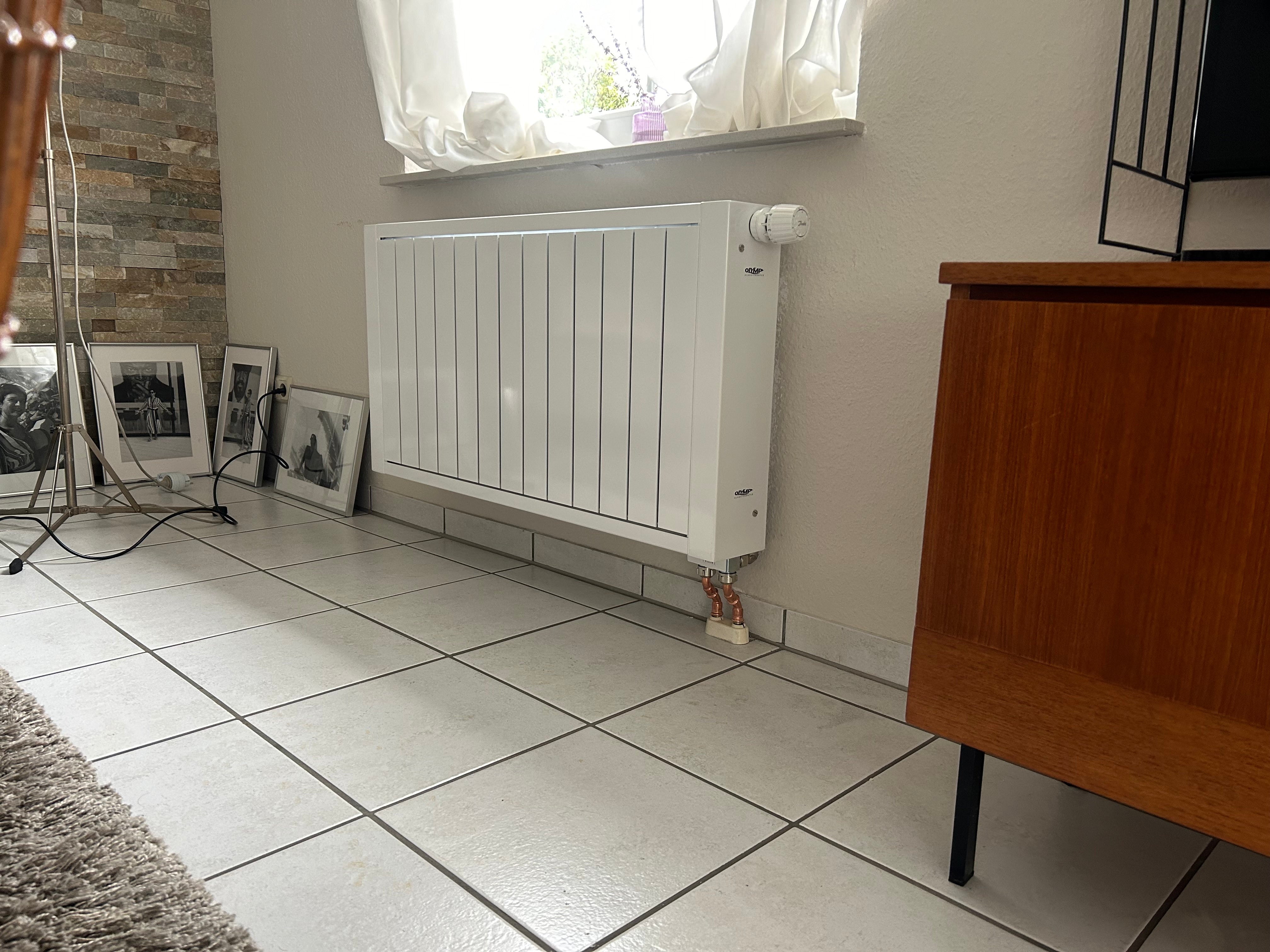 Ein Heizkörper hängt an der Wand und um ihn herum sind Gegenstände aus einem Wohnzimmer.