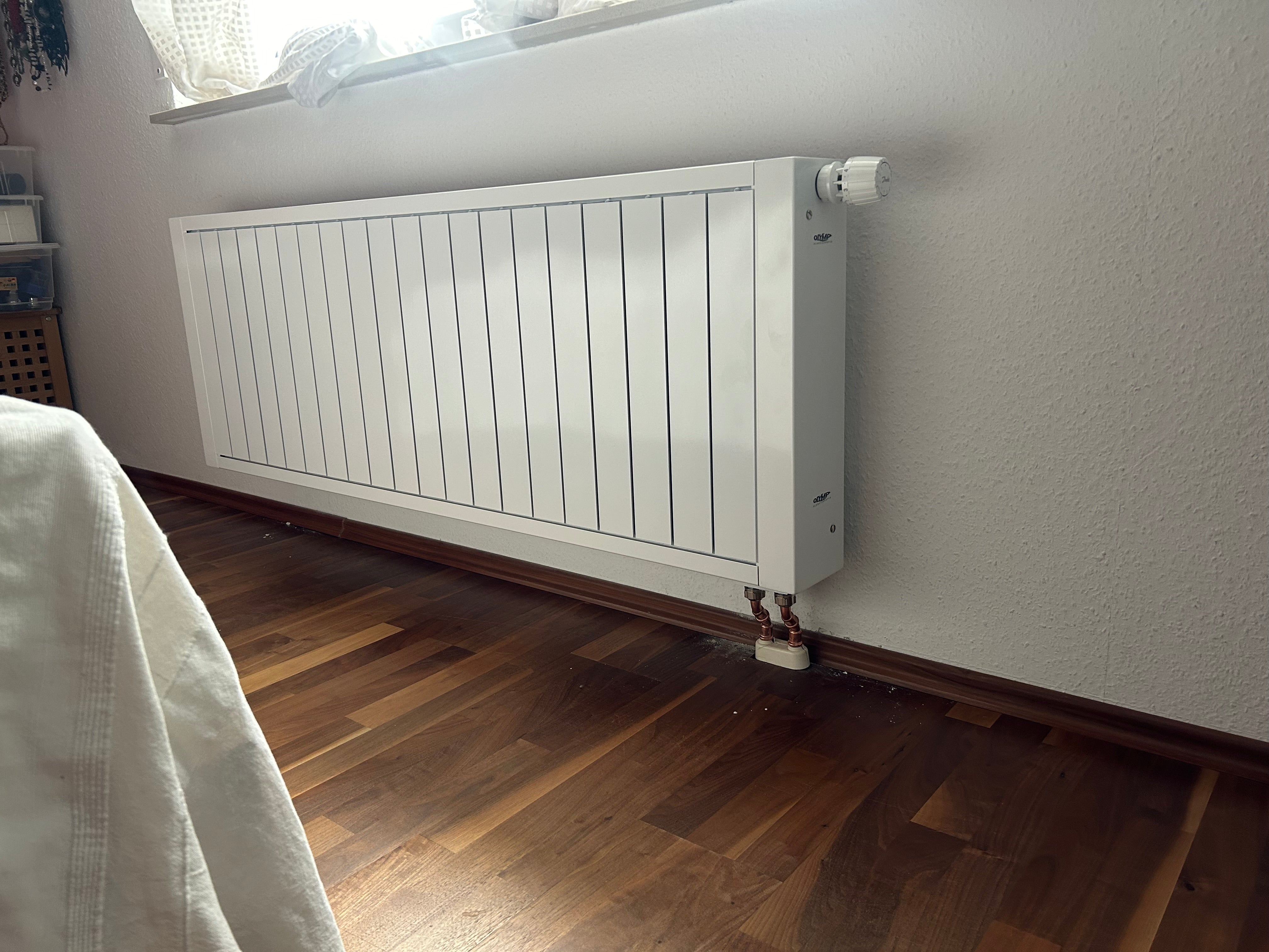 Ein Heizkörper ist unter einem Fenster, durch das das Licht scheint.