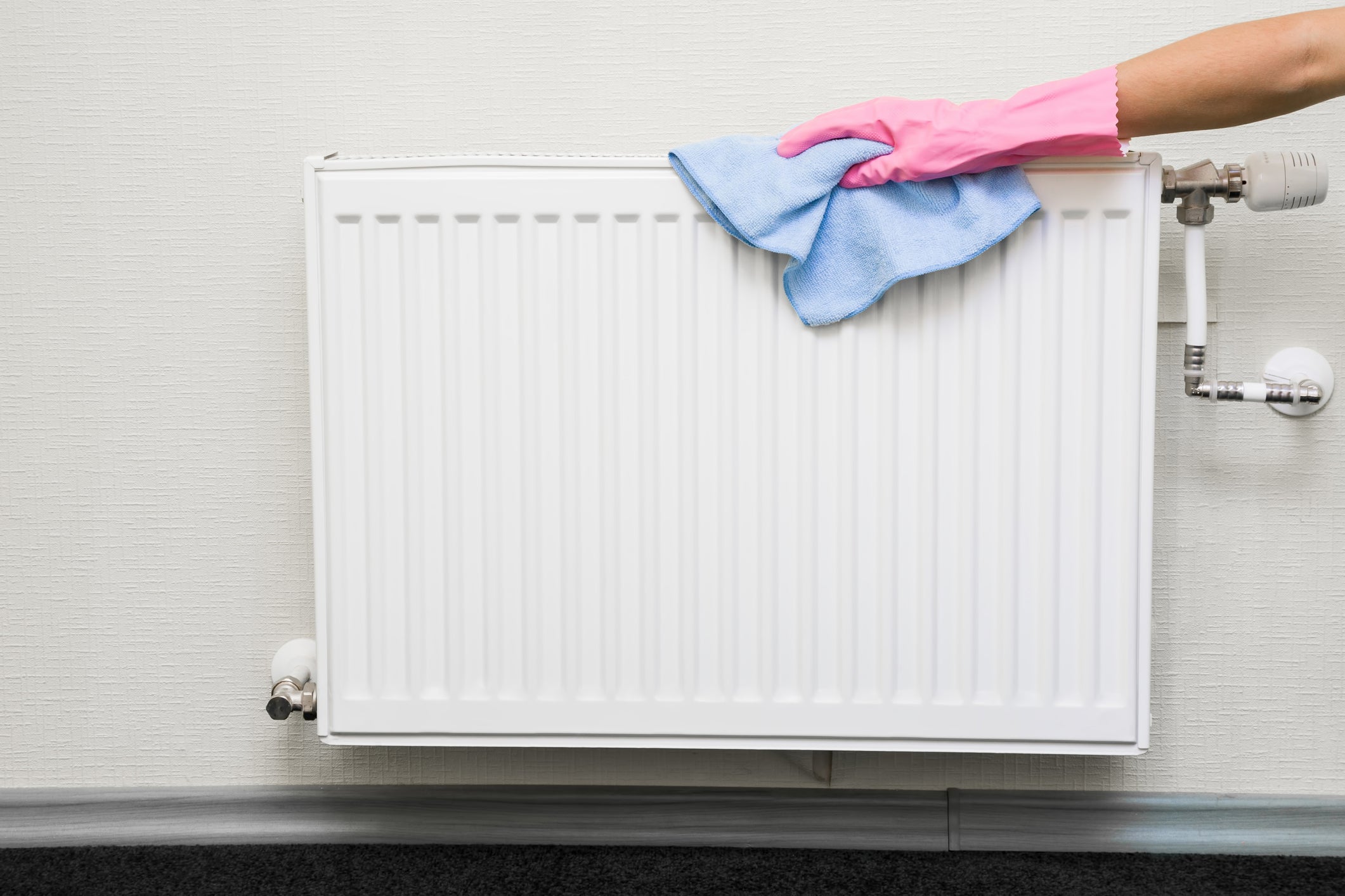 Eine Person mit Gummihandschuhen reinigt einen Heizkörper.